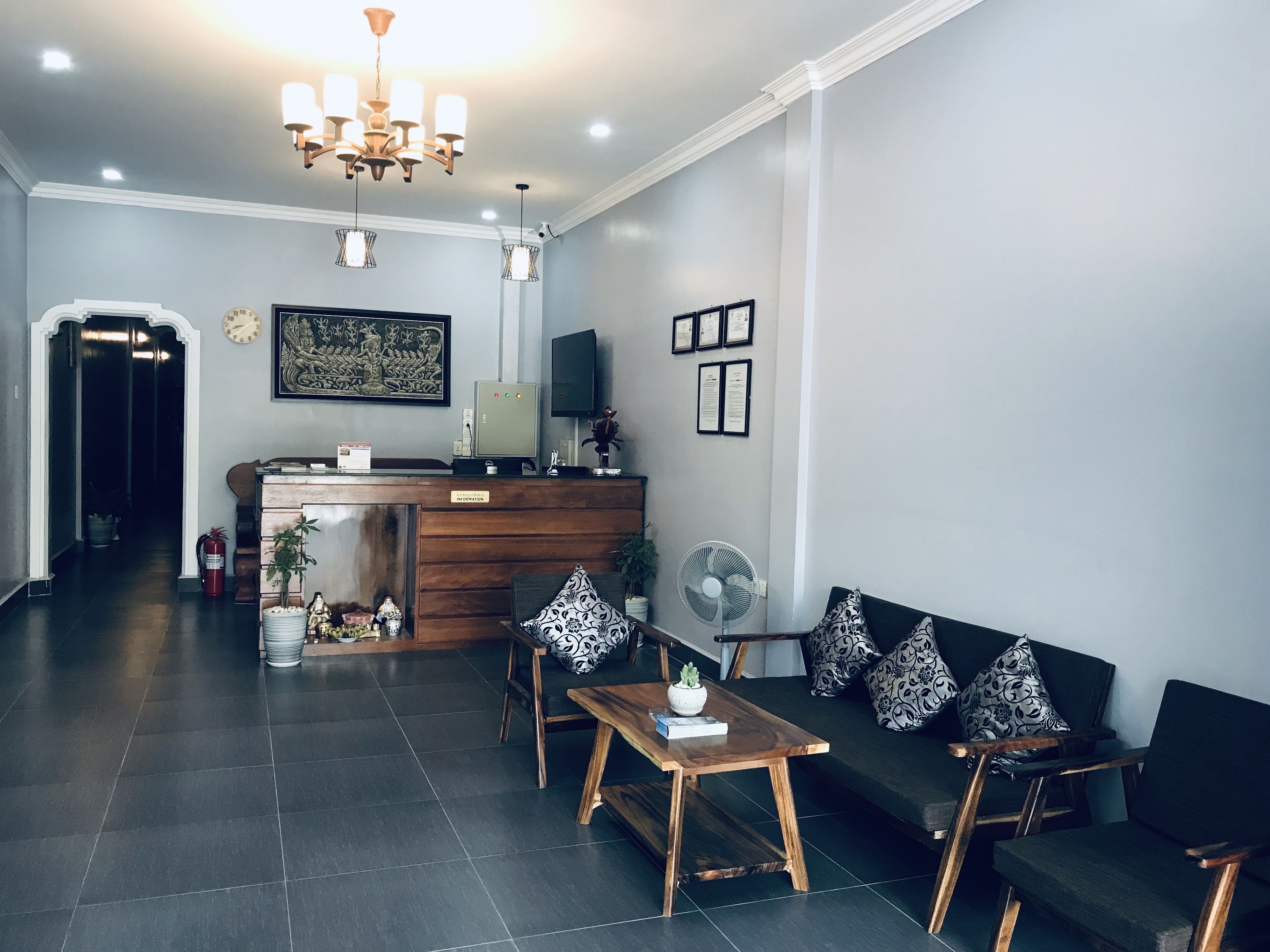 A reception area with a wooden desk, a sofa with patterned cushions, a fan, and a chandelier.