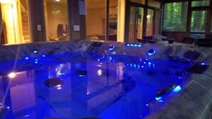 A hot tub with blue lighting, surrounded by seating and large windows.