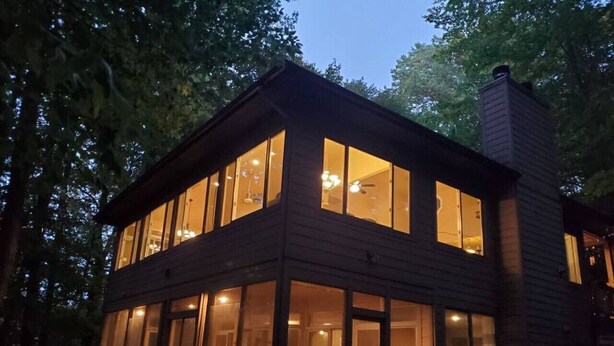 A two-story wooden cabin with large windows, a chimney, and a deck area.