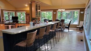 A modern kitchen with a long island counter, bar stools, and a dining area with a chandelier.