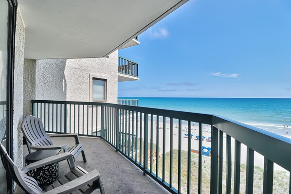 A balcony with a view of the beach, a table, and two chairs. - Ocean Bay Club 607 | Oceanfront Four Bedroom Condo (North Myrtle Beach)
