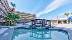 Una piscina amb un pont, palmeres i un edifici amb balcons.