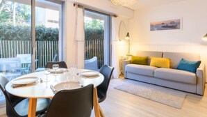 Un coin repas avec une table ronde dressée pour quatre personnes, un canapé avec des coussins et une grande fenêtre donnant sur un paysage verdoyant.