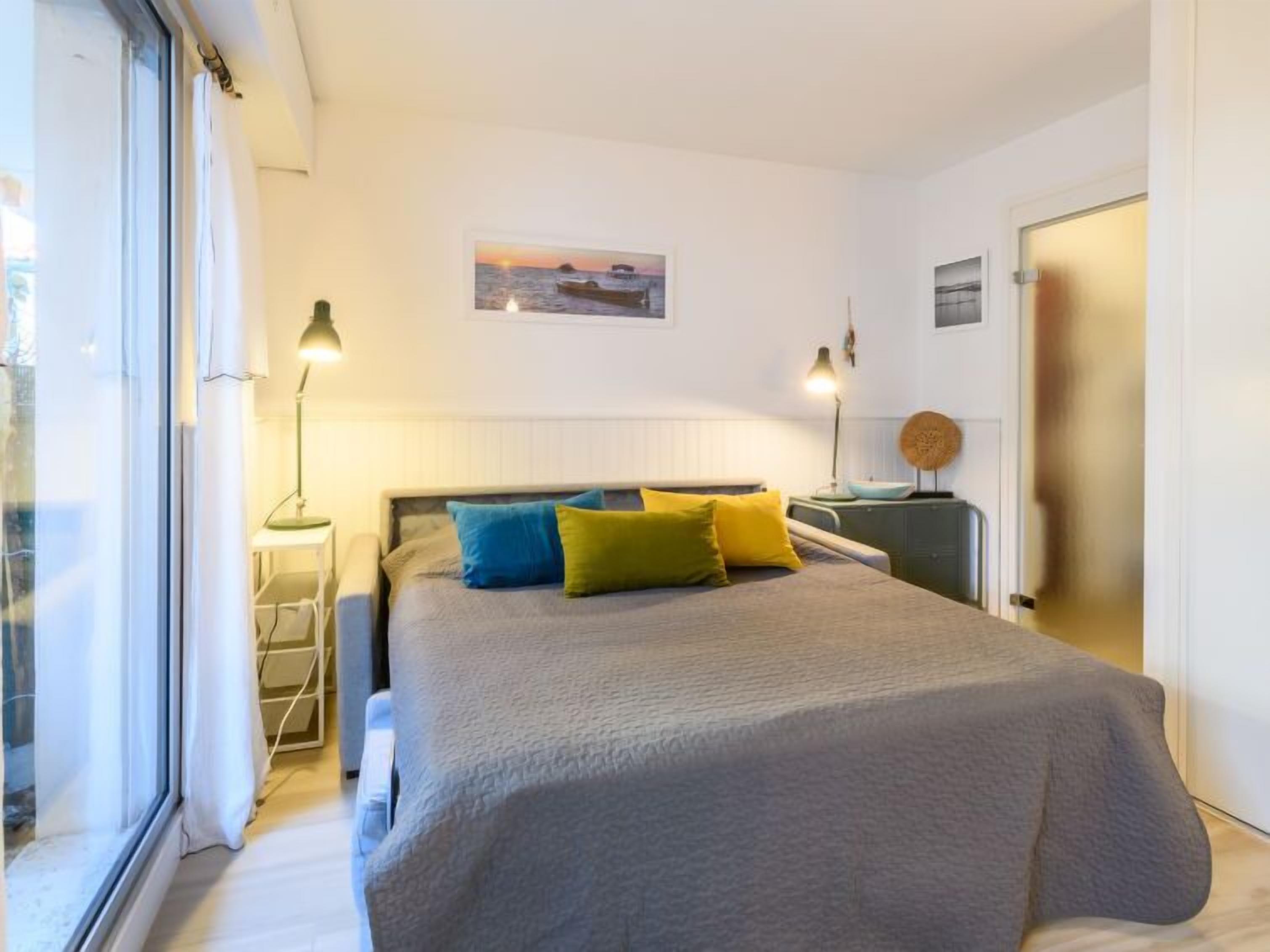 A bedroom with a bed, bedside lamps, a bedside table, a window, and a wall-mounted picture.