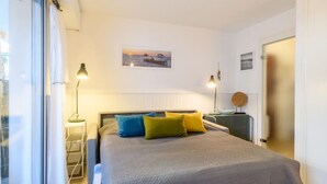 Une chambre à coucher comprenant un lit, des lampes de chevet, une table de chevet, une fenêtre et un tableau accroché au mur.
