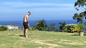 En man spelar golf på en gräsklädd golfbana med utsikt över havet.