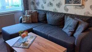 Un salon chaleureux avec un canapé d’angle, une table basse en bois et un mur orné d’un motif floral.