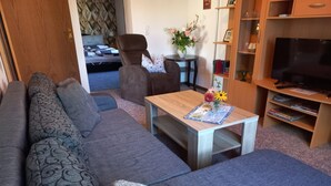 Un salon moderne comprenant un canapé, une table basse agrémentée d’un arrangement floral, un meuble TV avec un téléviseur à écran plat et une bibliothèque.