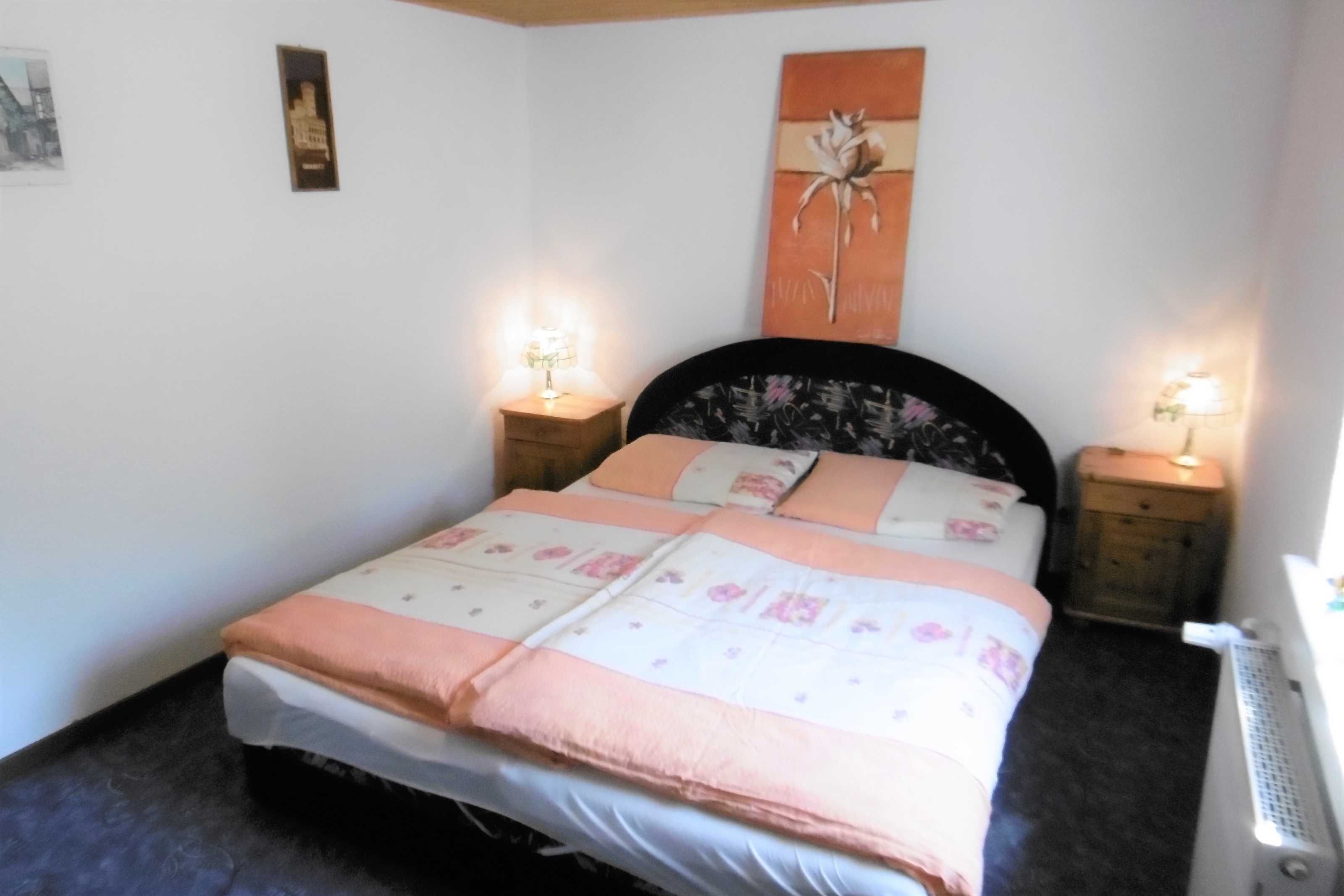 A neatly made bed with a floral bedspread, two bedside lamps, and a wall-mounted artwork.