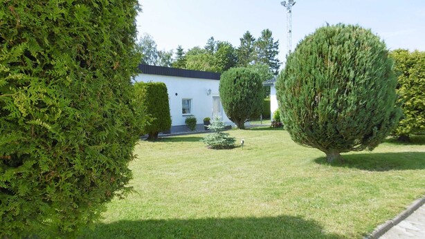 Un jardin bien entretenu, avec des haies soigneusement taillées et un bâtiment blanc surmonté d’un toit noir.