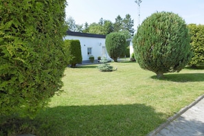 Um jardim bem cuidado com sebes aparadas e um edifício branco com telhado preto.