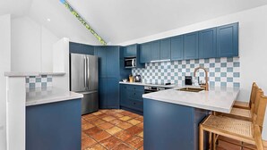 Eine kleine Küche mit blauen Schränken, einem Edelstahlkühlschrank, einer Mikrowelle und einer karierten Spritzschutzwand.