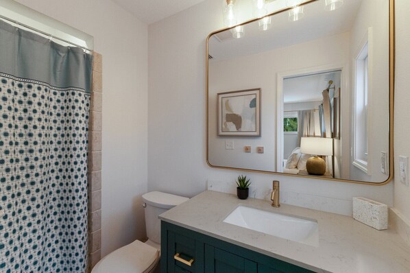 A bathroom with a white sink, a mirror with a gold frame, a toilet, and a shower curtain with a polka dot pattern.
