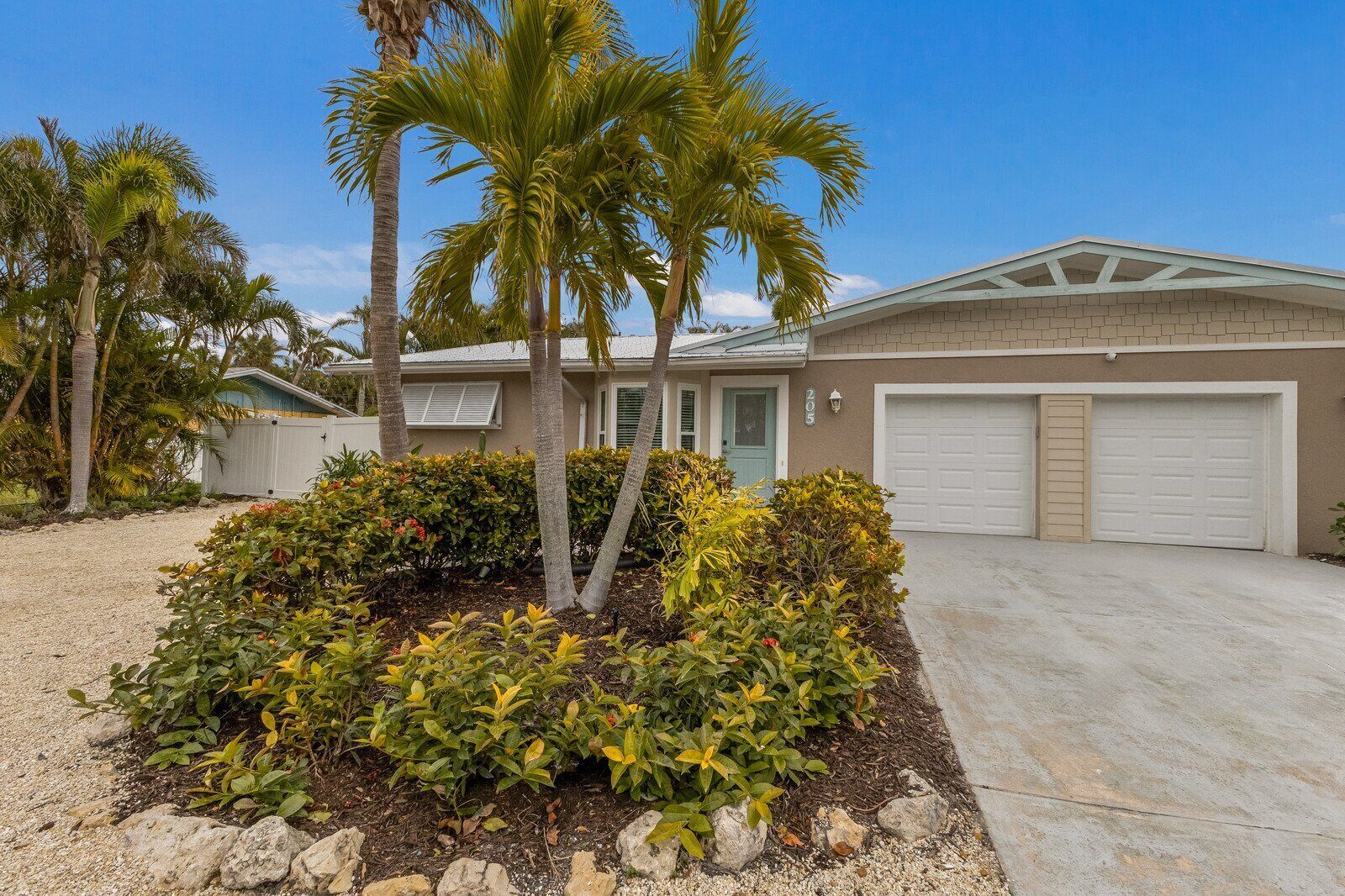 A two-story house with a garage, surrounded by palm trees and a landscaped garden.