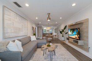 A modern living room with a grey sectional sofa, a wooden coffee table, and a flat-screen TV on a wooden wall.