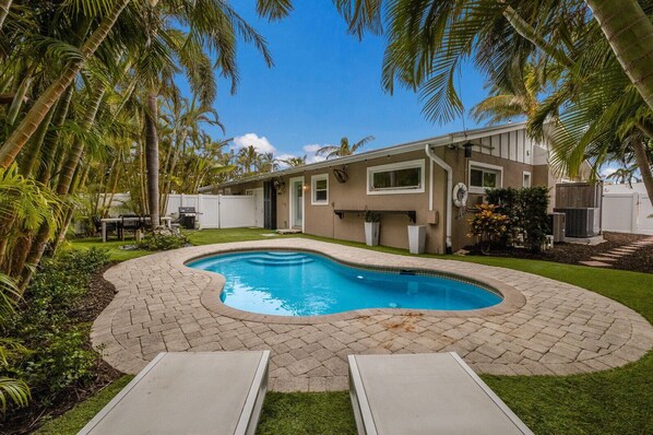 A swimming pool with a curved edge, surrounded by a brick patio and palm trees.