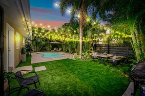 A backyard with a swimming pool, outdoor furniture, and string lights.