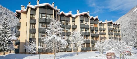 A multi-story hotel with balconies, surrounded by snow-covered trees and a clear sky.