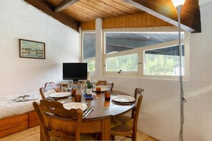 A dining area with a wooden table set for four, a television, and a window with a view of trees. - Résidence Grand Roc - Bruyères 441, Argentière (Chamonix), France (Argentière (Chamonix))