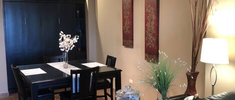 A dining area with a black table and chairs, a vase with white flowers, and a decorative vase with green foliage.