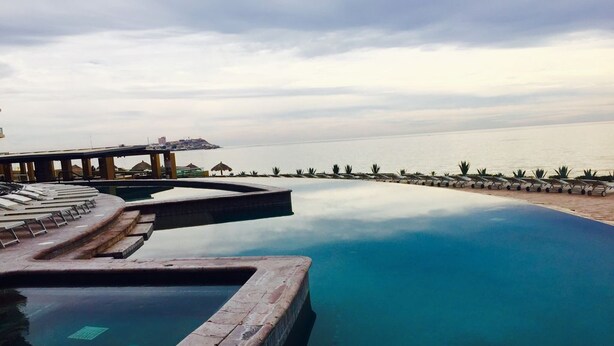 Une piscine avec vue sur la mer, un pont et des chaises longues.