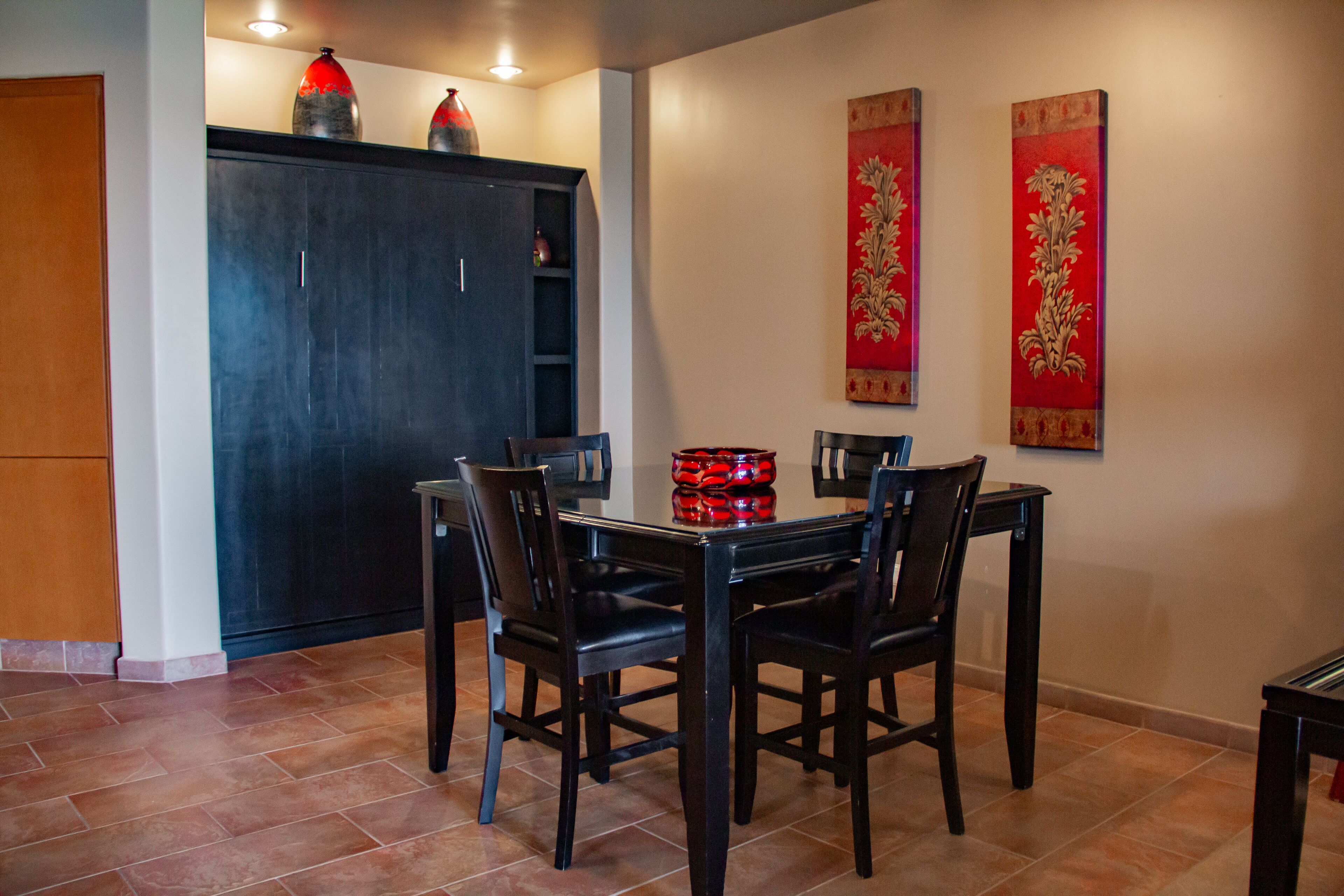 Zona pranzo con tavolo e sedie in legno scuro, un armadio con oggetti decorativi e due arazzi rossi.