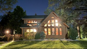 A two-story house with a wooden exterior, a visible deck, and a well-maintained lawn. - Beautiful Beachfront Custom Log Cabin on Lake Huron (Oscoda)
