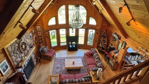A spacious loft with a high ceiling, large windows, a fireplace, and a cozy seating area. - Beautiful Beachfront Custom Log Cabin on Lake Huron (Oscoda)
