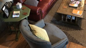 Una sala de estar con un sofá de cuero rojo, un sillón gris, una mesa de centro de madera y una mesita auxiliar con una lámpara.