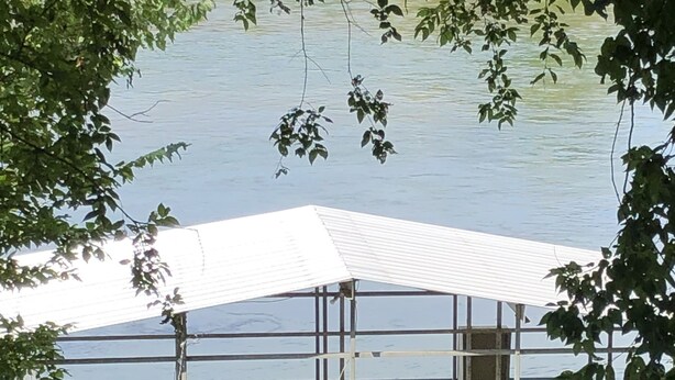 Un muelle de madera con un área de descanso techada, dos sillas y una pequeña mesa.