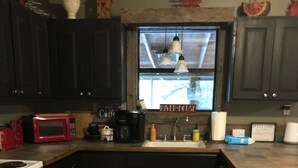 Una cocina con armarios oscuros, una estufa blanca, un microondas rojo, una cafetera y un ventanal con vistas a un edificio.