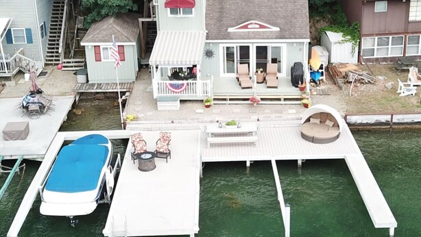 Une propriété située au bord de l’eau, dotée d’un quai, d’un petit bateau et d’une maison avec une véranda et un espace salon extérieur.