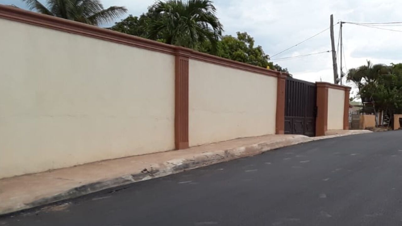 Una calle con un muro color beige y una verja negra.