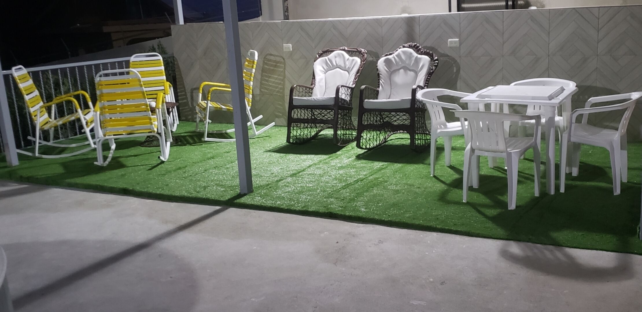 Espace extérieur aménagé avec des chaises et une table, entouré d’une zone de gazon synthétique verdoyant.