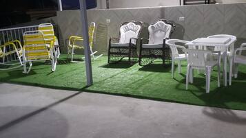 Espace extérieur aménagé avec des chaises et une table, entouré d’une zone de gazon synthétique verdoyant.