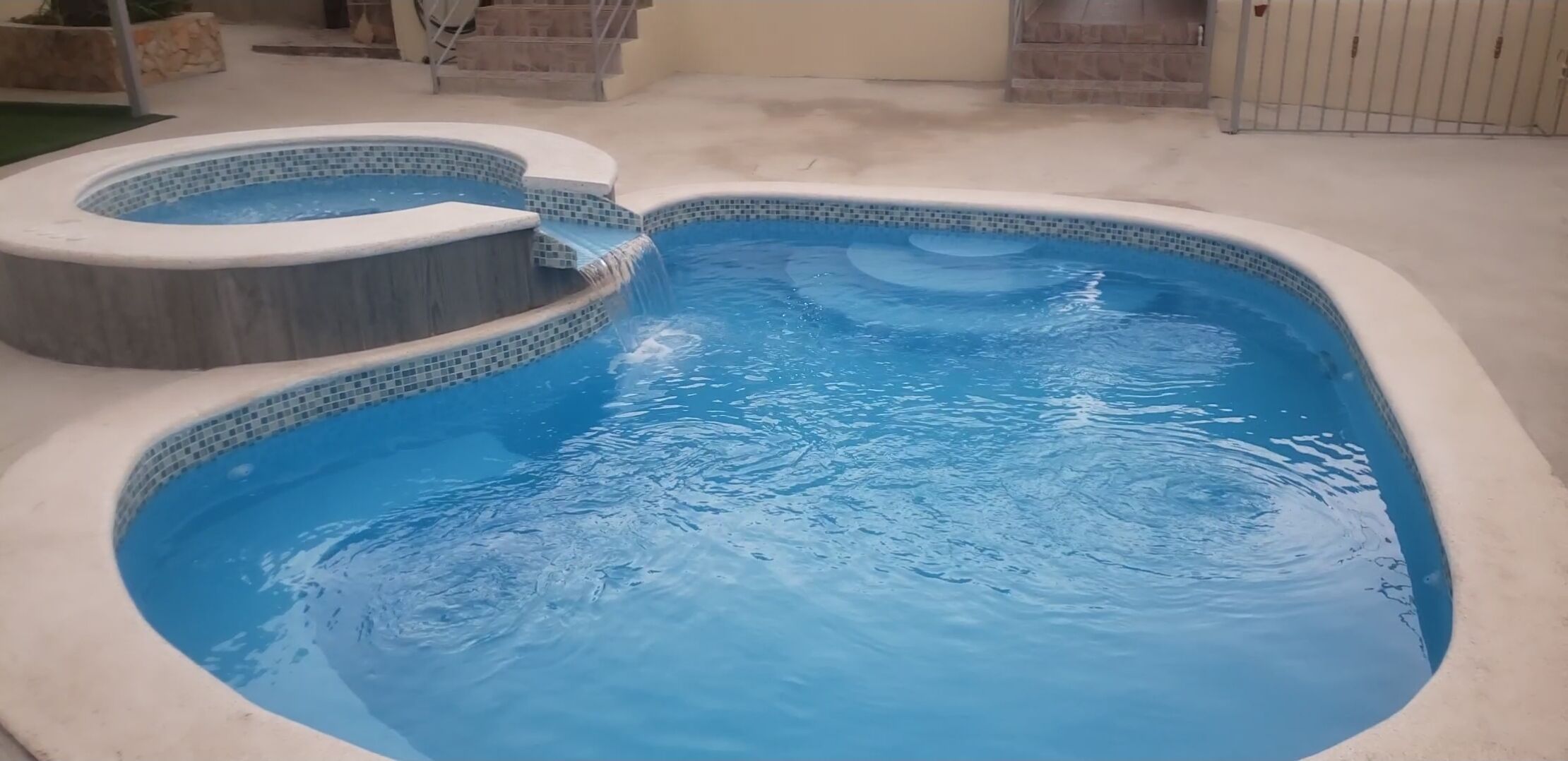Una piscina con una pequeña cascada y una zona de hidromasaje separada.