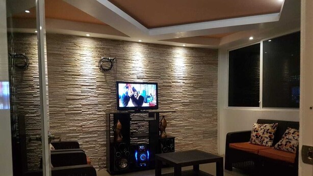 A modern living room with a stone-textured wall, a flat-screen TV, a gaming console, and a sofa with patterned cushions.