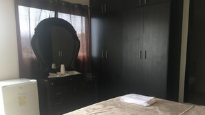 A bedroom with a bed, a dresser, a mirror, and a refrigerator.