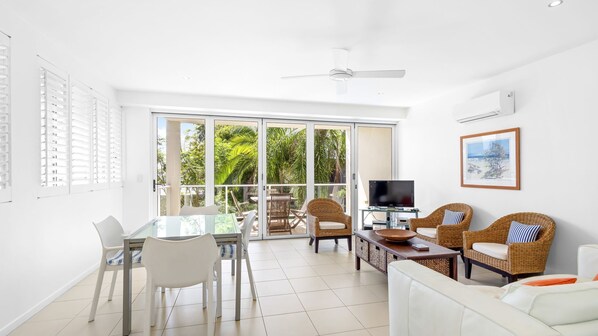 A bright living room with a glass door leading to a balcony, wicker furniture, a flat-screen TV, and a framed picture on the wall. - No. One Park 4 Sunshine Beach (Sunshine Beach)