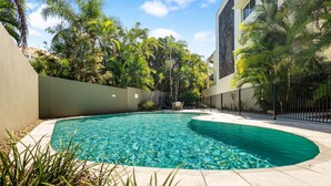 A swimming pool with clear water, surrounded by a low wall and palm trees. - No. One Park 4 Sunshine Beach (Sunshine Beach)