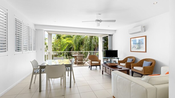 A modern living room with a glass table, white chairs, a sofa, and a TV. - No. One Park 4 Sunshine Beach (Sunshine Beach)