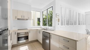 A modern kitchen with white cabinetry, stainless steel appliances, a large window, and a view of greenery outside. - No. One Park 4 Sunshine Beach (Sunshine Beach)
