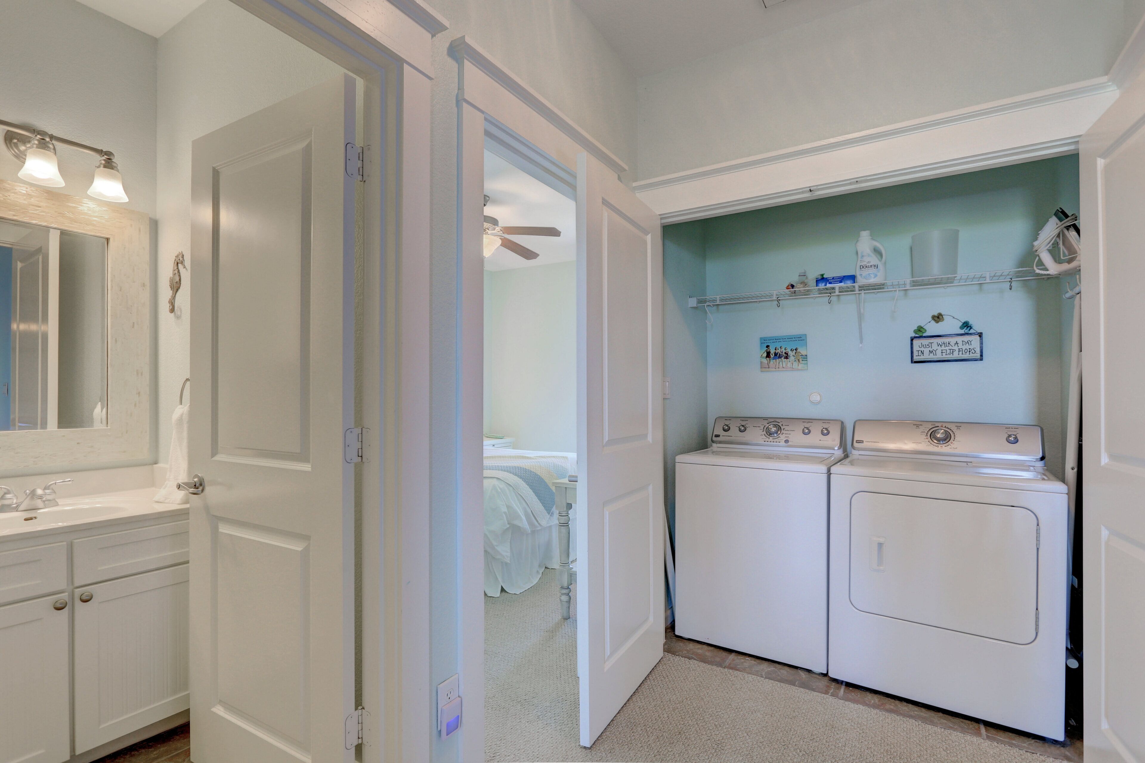 A laundry room with two washing machines, a mirror, and a shelf with laundry supplies.