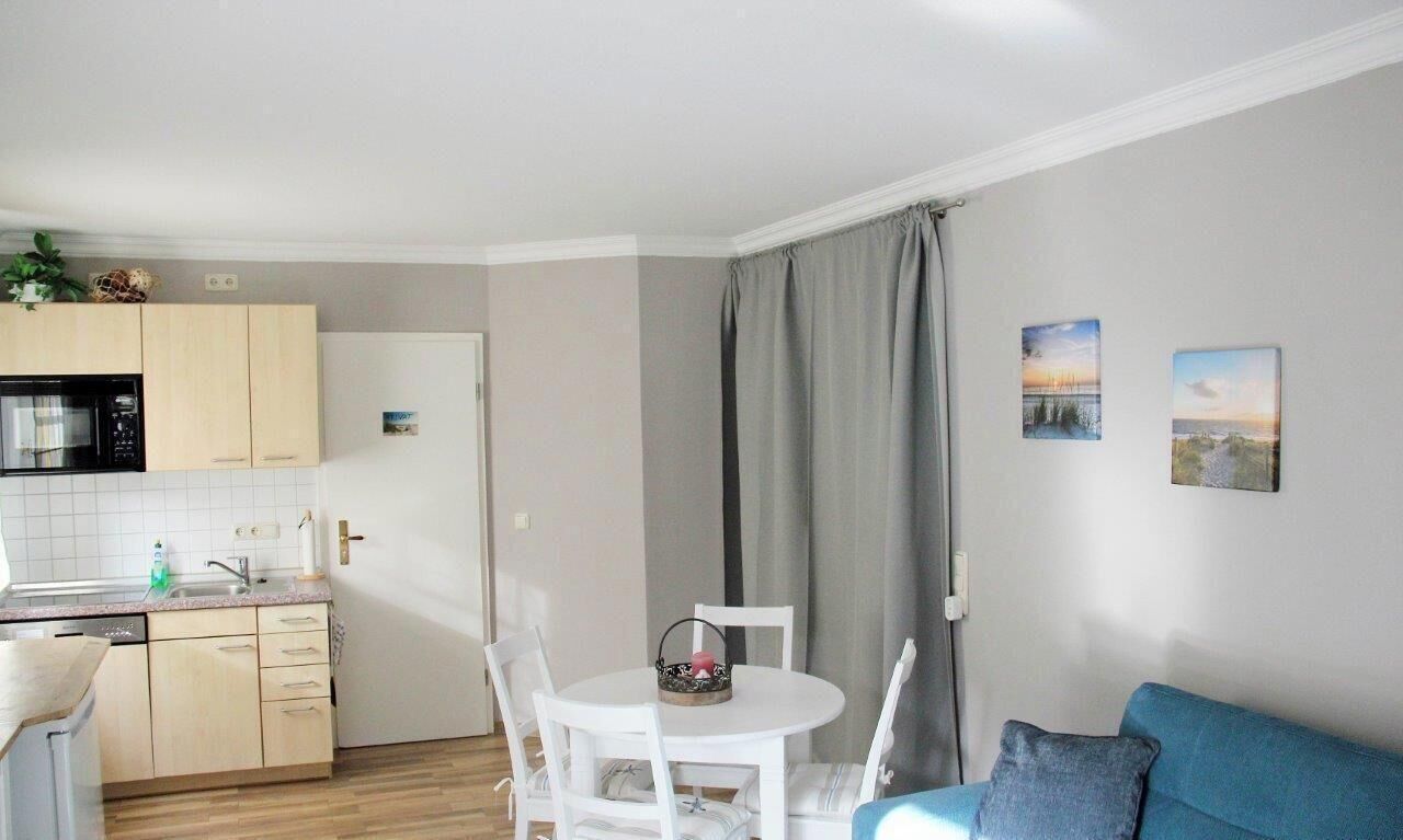 A compact living space with a kitchenette, a dining area with a white table and chairs, a blue sofa, and two landscape paintings on the wall.