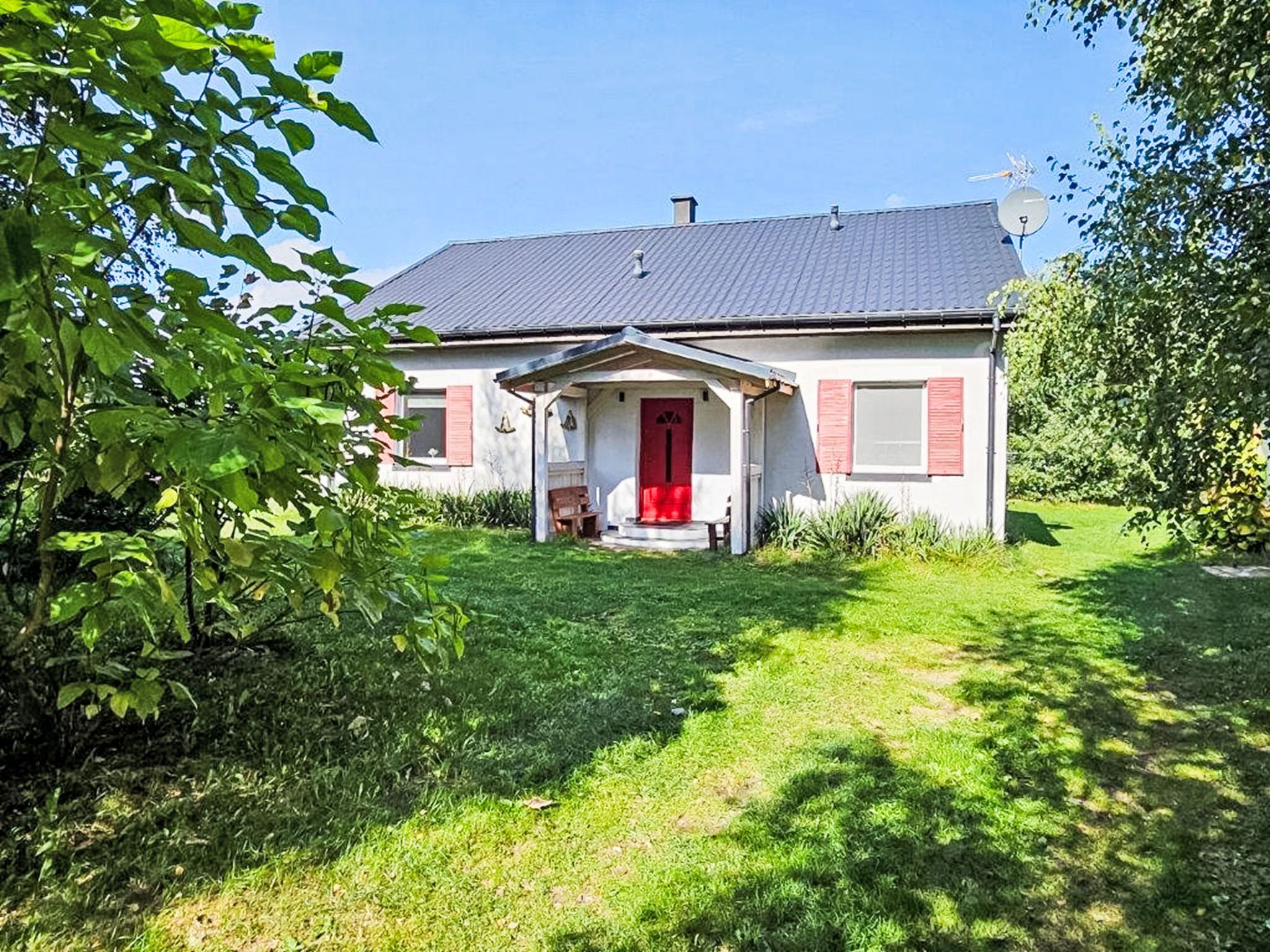 Ein zweistöckiges Haus mit roter Tür, einer Satellitenschüssel und einer kleinen Veranda.