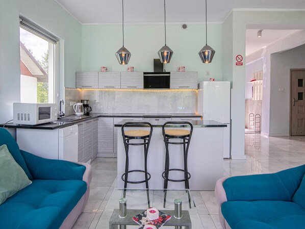 Een moderne keuken met een centraal eiland, twee barkrukken en een eettafel met stoelen.