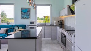 Une cuisine moderne dotée d’un îlot central, d’appareils électroménagers en acier inoxydable et offrant une vue sur un paysage verdoyant grâce à de grandes fenêtres.