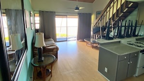 Un amplio salón con piso de madera, una mesa de comedor con sillas, una zona de cocina con estufa y una escalera que sube a un nivel superior.