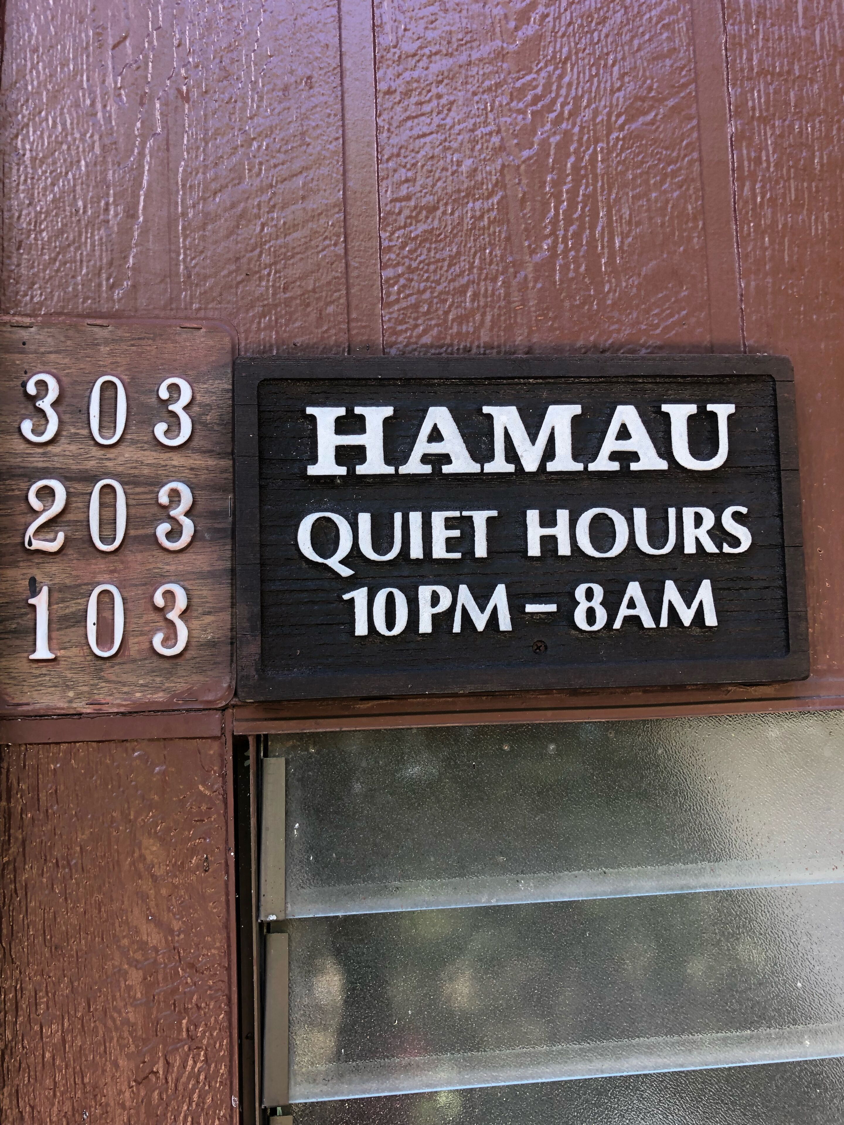 Letrero con el texto 'HAMAU QUIET HOURS 10PM-8AM' y el número '303' sobre un fondo de madera.