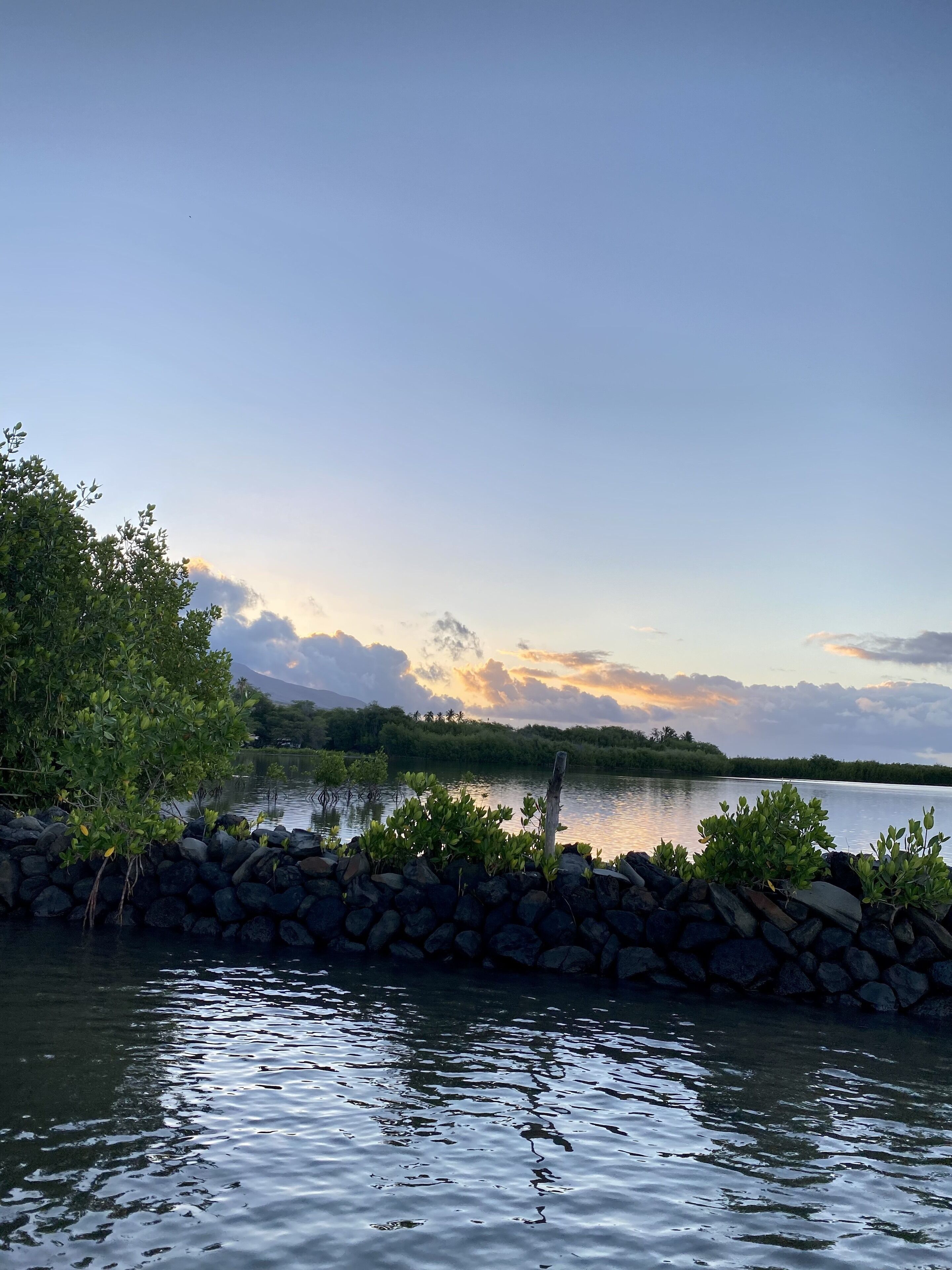 A calm lake with a stone wall in the foreground and a forested landscape in the background.